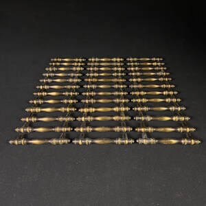 May include: A set of 36 antique brass cabinet pulls with a simple, elegant design. Each pull has a slightly curved shape with a decorative knob on each end.