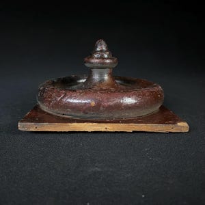 May include: A dark brown wooden finial with a square base and a rounded top. The finial has a decorative, pointed top and a smooth, polished finish.