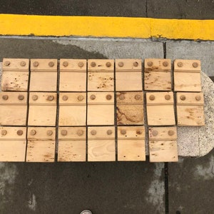 May include: A set of 18 wooden tiles with a light brown finish. Each tile has four evenly spaced holes with a small, round, wooden knob in each hole.
