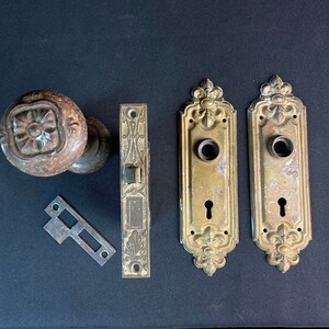 May include: Antique brass door hardware set with a decorative floral design. The set includes a door knob, two door plates, a latch, and a strike plate.
