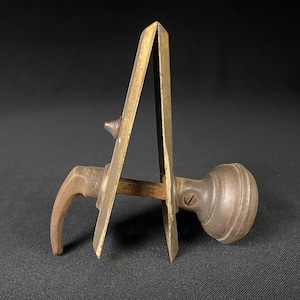 May include: A vintage door knob with a brass finish and a hook-shaped handle. The knob is attached to a metal plate with a decorative design.