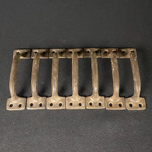 May include: Eight antique brass door pulls with a simple, curved design. Each pull has two holes for mounting.