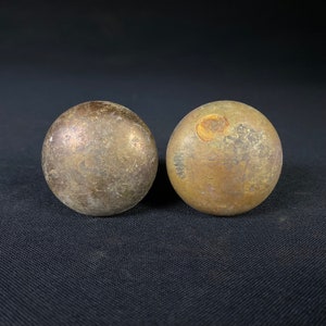 May include: Two round, brass door knobs with a worn, aged finish. The knobs have a slightly uneven surface and a dull, golden color.
