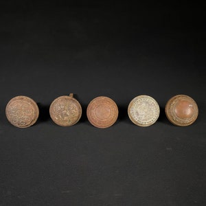 May include: Five antique door knobs with intricate designs. The knobs are made of metal and have a worn, aged finish. They are all different shapes and sizes, but they share a similar style.