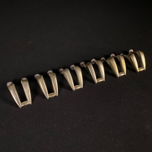 May include: A set of eight silver-toned metal drawer pulls with a simple, modern design. The pulls are all the same size and shape, and they have a slightly curved shape.