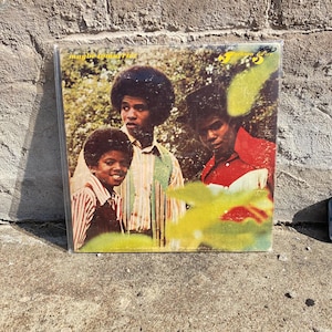 May include: A vintage vinyl record album cover featuring The Jackson 5. The album cover has a photo of the group in front of a green background. The album title is "Maybe Tomorrow". The Jackson 5 are wearing various shirts.