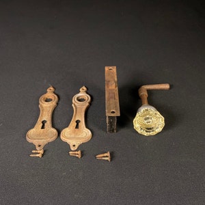 May include: Two antique brass keyhole escutcheons with a decorative design and a single antique brass door knob with a clear glass knob.