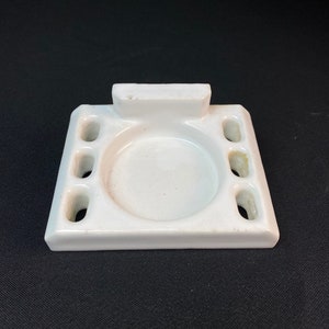 May include: White ceramic toothbrush holder with four toothbrush slots and a round soap dish.
