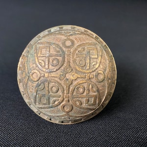 May include: A round, brass door knocker with an intricate, geometric design. The knocker is a deep, golden color and has a raised, circular pattern.