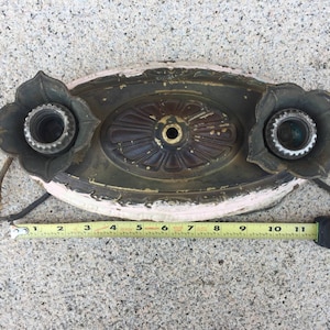 May include: An antique ceiling light fixture with two sockets and a decorative floral design. The fixture is made of metal and has a white and pink finish. It measures approximately 10 inches in length.