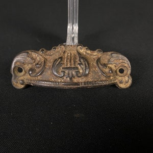 May include: A vintage, ornate, cast iron drawer pull with a decorative, floral design. The pull is dark brown and has two holes for mounting.
