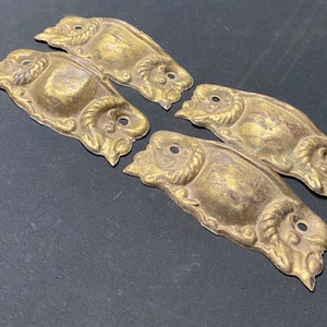 May include: Four antique brass decorative hardware pieces with ornate designs. Each piece has a raised, oval-shaped center with a detailed floral pattern.