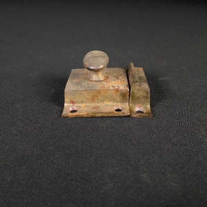 May include: A vintage, rusty metal latch with a round knob. The latch is made of two pieces, one with a knob and the other with a hook. The latch is in a worn condition, with signs of rust and wear.