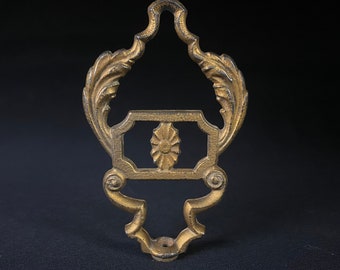May include: Ornate, antique-style metal bracket in a gold finish. The bracket features a decorative floral design in the center and leaf-like accents. The bracket is approximately 6 inches tall.