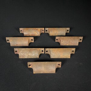 May include: Seven antique metal drawer pulls with a rustic brown finish. The pulls are shaped like a half-circle with rounded edges and have two holes for mounting.