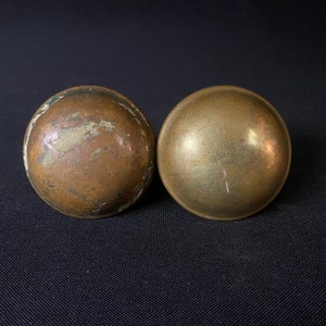 May include: Two round, brass door knobs. One knob has a smooth, polished finish, while the other has a more textured, aged finish.