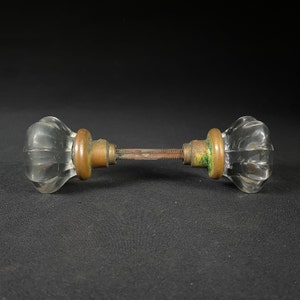May include: A pair of antique glass door knobs with brass accents. The knobs are clear glass with a faceted design and have a brass backplate and screw.