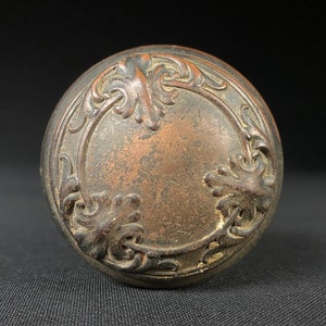 May include: A vintage, ornate, bronze door knob with a circular design featuring intricate floral and scrollwork.