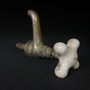 May include: A vintage brass faucet with a white porcelain handle marked "COLD". The faucet is worn and has a patina finish.
