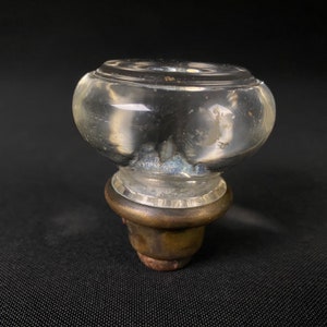 May include: A clear glass door knob with a brass base. The knob has a textured surface and a slightly cloudy appearance.