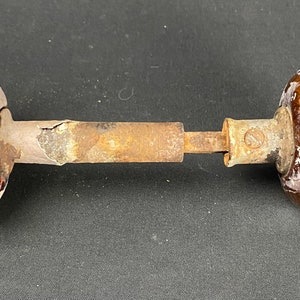 May include: A vintage door knob with a brown and white ceramic design on one side and a white ceramic design on the other side. The knob is attached to a metal rod.