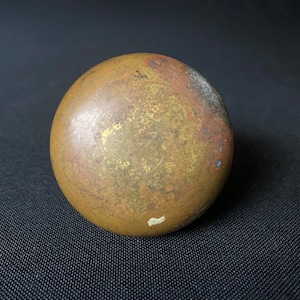 May include: A round, brass door knob with a worn, aged finish. The knob has a slightly uneven surface with a patina of age.