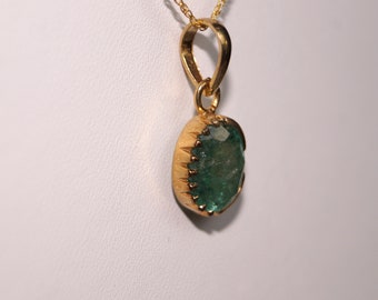 May include: A gold pendant with a large, oval-shaped green gemstone. The gemstone is set in a gold bezel with a decorative edge.