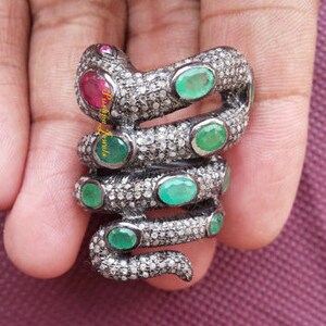 Può includere: Un anello a forma di serpente in argento con pietre preziose verde smeraldo e rosso rubino. Il serpente è avvolto attorno a un dito ed è incastonato con piccoli diamanti.