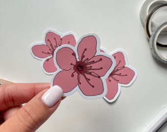 May include: Pink flower sticker with a white outline. The sticker has a five-petal flower with a red center and a white background.
