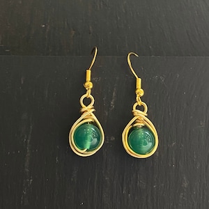 May include: A pair of gold earrings with green gemstone beads. The beads are wrapped in gold wire and dangle from gold hooks.