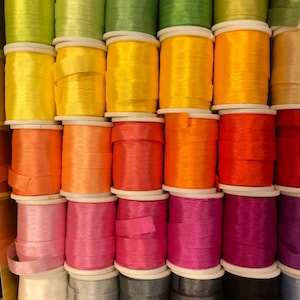 May include: A collection of spools of colorful thread, arranged in rows. The thread colors include green, yellow, orange, pink, white, gray, and black.