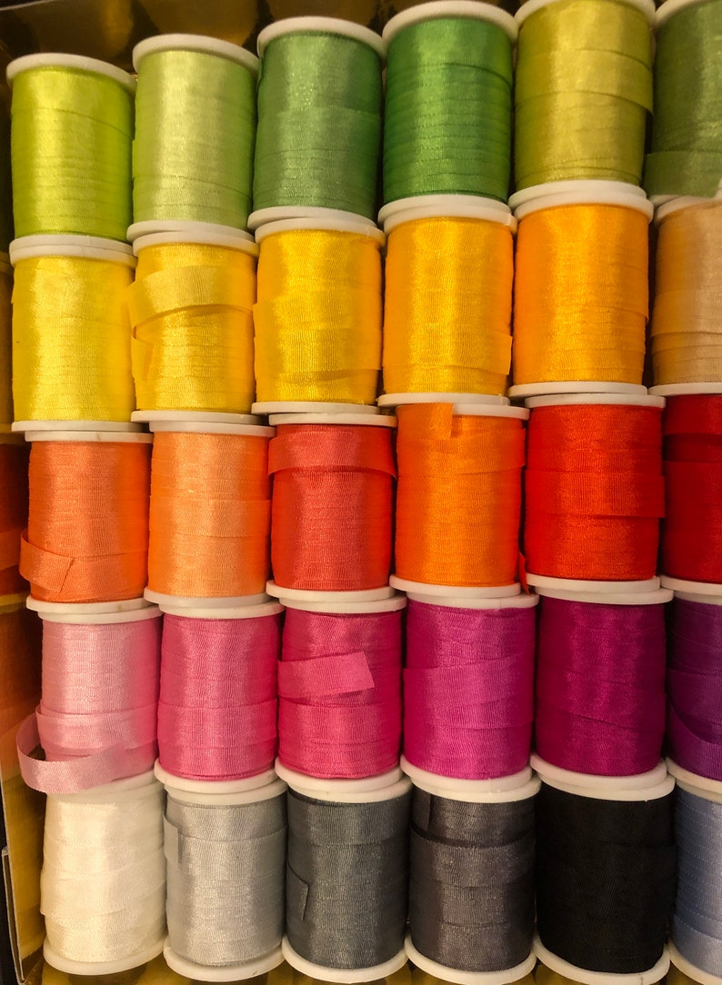 May include: A collection of spools of colorful thread, arranged in rows. The thread colors include green, yellow, orange, pink, white, gray, and black.