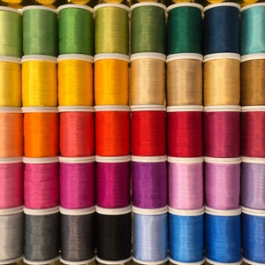 May include: A collection of spools of thread in various colors, including green, yellow, orange, red, pink, purple, blue, gray, and black.