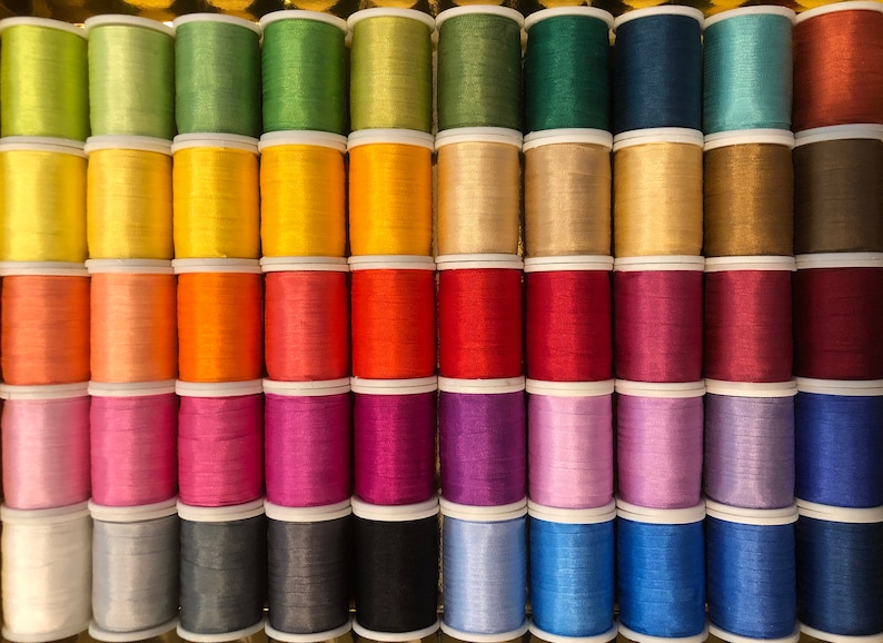 May include: A collection of spools of thread in various colors, including green, yellow, orange, red, pink, purple, blue, gray, and black.