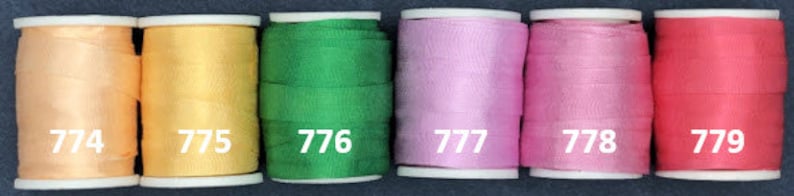 May include: Six spools of thread in different colors. The spools are labeled with numbers 774, 775, 776, 777, 778, and 779.
