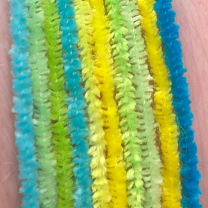 May include: A close-up of a bracelet made with colorful pipe cleaners. The bracelet is made with blue, yellow, and green pipe cleaners. The pipe cleaners are arranged in a striped pattern.