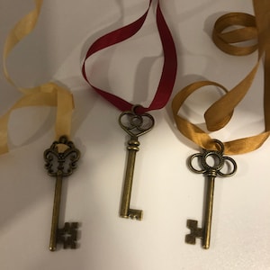 May include: Three antique-style keys with different decorative tops, each attached to a ribbon. The ribbons are gold, red, and beige.