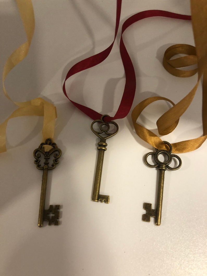 May include: Three antique-style keys with different decorative tops, each attached to a ribbon. The ribbons are gold, red, and beige.