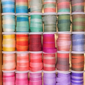 May include: A collection of 36 spools of colorful silk ribbon, arranged in a wooden box. The ribbons are in various shades of blue, green, yellow, orange, red, pink, purple, and brown.