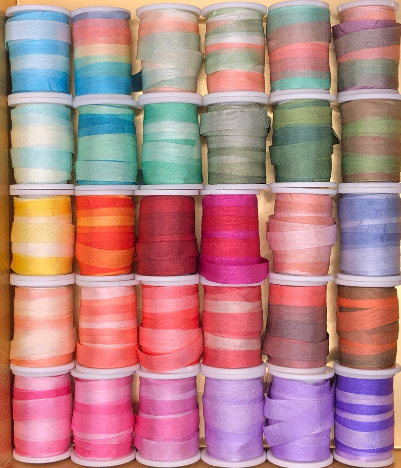 May include: A collection of 36 spools of colorful silk ribbon, arranged in a wooden box. The ribbons are in various shades of blue, green, yellow, orange, red, pink, purple, and brown.