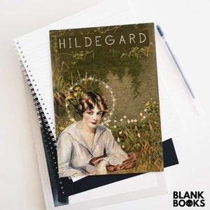 May include: A notebook with the title "HILDEGARD" on the cover, featuring a vintage illustration of a woman with a halo. The notebook is on top of other notebooks and a pen. The bottom right corner has the text "BLANK BOOKS".