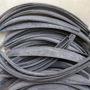 Puede incluir: Una pila de tiras de goma negra, todas dobladas en forma de curva. Las tiras están apiladas unas sobre otras, creando un aspecto desordenado y enredado.