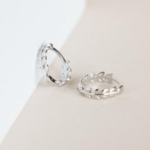May include: A pair of silver hoop earrings with a leaf design. The earrings are small and delicate.