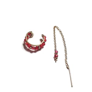 Peut inclure: Un ensemble composé d'un ear cuff doré et d'une boucle d'oreille fil. L'ear cuff est une bande incurvée ornée de petites pierres précieuses rouges. La boucle d'oreille fil présente une chaîne délicate avec des accents de pierres précieuses rouges assorties et une barre droite.