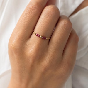Peut inclure: Une bague fine en or composée d'un anneau délicat orné d'une série de petites perles rondes en rubis rose foncé, alternées avec une perle en or polie, formant un bijou discret et élégant pour le doigt.