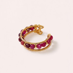 Peut inclure: Une bague ouverte dorée composée de deux anneaux parallèles reliés par un détail en fil torsadé. La bague est ornée d'une rangée de petites perles rondes à facettes dans des tons magenta, fuchsia et rose foncé, séparées par de minuscules entretoises dorées.