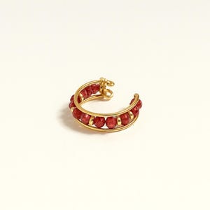 Peut inclure: Un ear cuff doré orné de petites perles rouges rondes. Le bijou a une forme incurvée conçue pour s'adapter à l'oreille. Les perles sont espacées uniformément, offrant un contraste vif avec l'or.