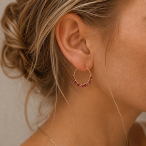 Peut inclure: Une fine créole en or ornée d'une série de petites perles rondes en pierre précieuse rose foncé fixées le long de la courbe inférieure de la monture circulaire en fil métallique. La boucle d'oreille présente une fermeture à crochet simple.