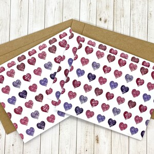 May include: Set of three blank greeting cards with a white background and a repeating pattern of pink and purple watercolor hearts.