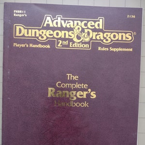 May include: A purple book cover with gold lettering. The title is "Advanced Dungeons & Dragons" with the subtitle "The Complete Ranger's Handbook". The book is a rules supplement for the 2nd edition of the game.